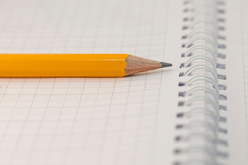 Note book and pencil. a pencil on a white paper in a cell. A simple pencil on a notebook in the cell. School supplies.