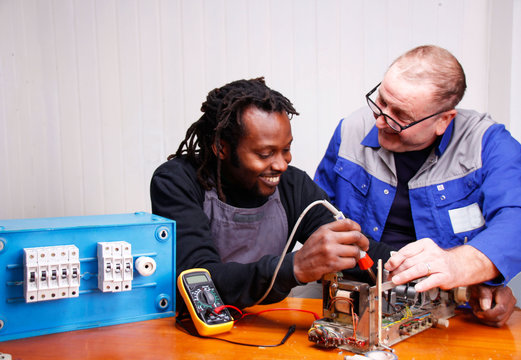 An experienced teacher teaching a young Electrician in the Workshop
