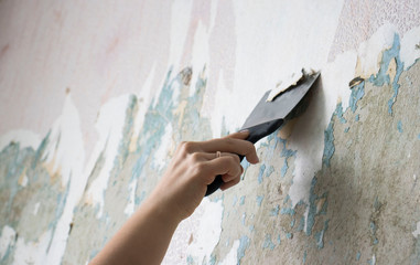 hand with a spatula cleans the wall from Wallpaper