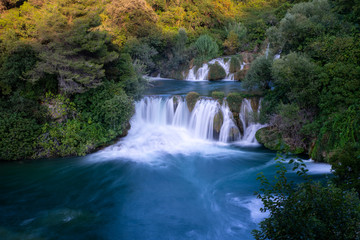 Waterfall at Krka, Croatia surrounded by green trees. Dark blue water.