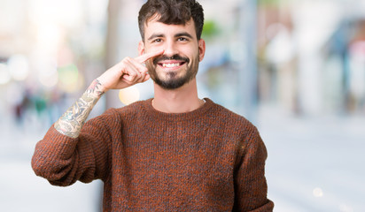 Young handsome man wearing winter sweater over isolated background Pointing with hand finger to face and nose, smiling cheerful