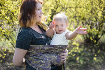 Mother wrapping her baby daughter in a sling for babywearing. Lifestyle image shot on location in a park on a sunny spring day. 
