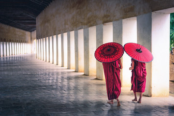 Two buddhist monk novice holding red umbrellas and walking in pagoda, Myanmar.