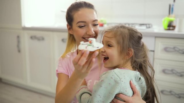 Happy mother tease her daughter with cookie playing on a kitchen