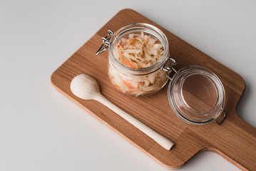 Cooking sauerkraut homemade recipe in a glass jar, wooden spoon and wooden culinary cutting board on a light background. Products at home