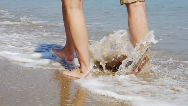 Close up of a young couple legs on romantic vacation walking on empty beach, slow motion