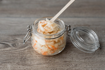 Fototapeta premium Homemade sauerkraut in a glass jar, wooden spoon on a wooden background. Delicious culinary shopping.