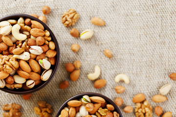 Mix of various nuts in a wooden cup against the background of fabric from burlap. Nuts as structure and background, macro. Top view.
