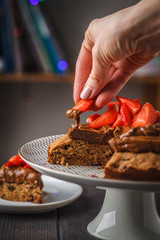 Vegan cake with dark chocolate, strawberries and chocolate cream on white dish, dark background.