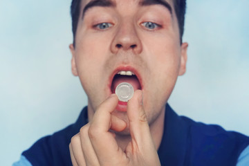 young man puts in his mouth a sucking pill for sore throat. Self-medication for flu and cold. Sick...