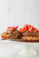 Vegan cake with dark chocolate, strawberries and chocolate cream on white dish.