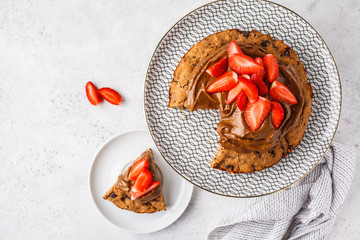 Vegan cake with dark chocolate, strawberries and chocolate cream on white dish.