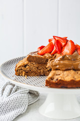 Vegan cake with dark chocolate, strawberries and chocolate cream on white dish.