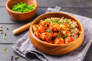 Chicken meatballs in tomato sauce with buckwheat in wooden bowl on dark wooden background.