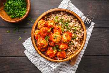 Chicken meatballs in tomato sauce with buckwheat in wooden bowl on dark wooden background.