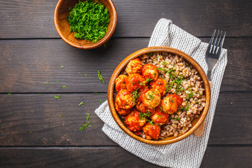 Chicken meatballs in tomato sauce with buckwheat in wooden bowl on dark wooden background, top view.