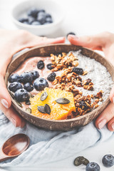 Breakfast smoothie bowl with chia pudding, berries and granola in a coconut shell on white wooden background.