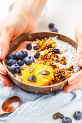 Breakfast smoothie bowl with chia pudding, berries and granola in a coconut shell on white wooden background.