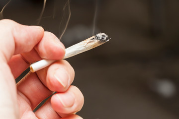Hand holding a lit, smoking marijuana cigarette
