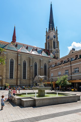 Naklejka premium Novi Sad, Serbia - May 27, 2018: View of one square with fountain and old buildings located behind at the Catholic Church `The Name of Mary Church