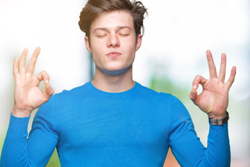 Young handsome man wearing blue sweater over isolated background relax and smiling with eyes closed doing meditation gesture with fingers. Yoga concept.