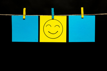 Copy space. Three stickers. In the middle is a yellow smiley with an expression of joy. Stickers are attached to the rope with clothespins.