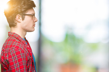 Young handsome student man wearing glasses over isolated background looking to side, relax profile pose with natural face with confident smile.