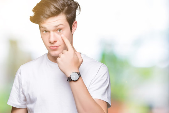 Young handsome man wearing casual white t-shirt over isolated background Pointing to the eye watching you gesture, suspicious expression