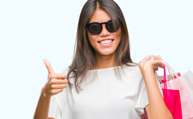 Young asian woman holding shopping bags on sales over isolated background happy with big smile doing ok sign, thumb up with fingers, excellent sign