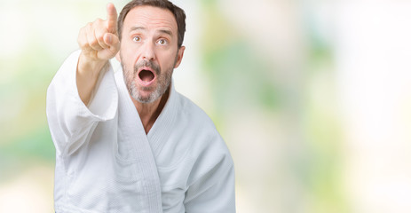 Handsome middle age senior man wearing kimono uniform over isolated background Pointing with finger surprised ahead, open mouth amazed expression, something in front