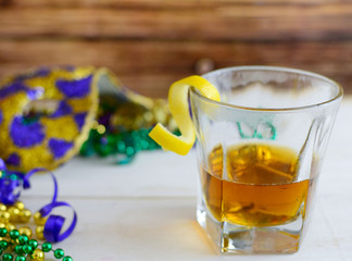 A sazerac cocktail with a lemon twist in a rocks glass on a wooden table. Mardi gras decorations around. Wooden background.