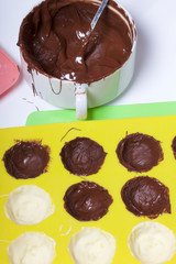 Melted black chocolate in white cups. Nearby silicone mold smeared with chocolate.