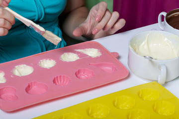 A woman using a brush brushes a melted chocolate silicone mold for dessert.