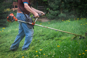 Gardener mowing grass by brushcutter in garden