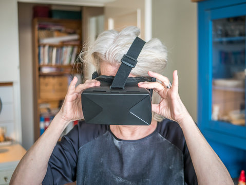 Senior woman is using VR, virtual reality headset at home.
