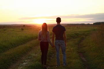 couple walking on the grass field at sunset
