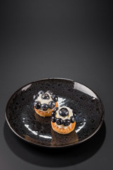 Two small cakes with blueberries and creamy cream on a black plate. Vertical. Copy space.