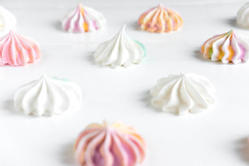 Pattern with meringues on a white wooden background. Multicolored meringues on a white background. Basis for confectionery banner, cafe, sweet shop. Meringue banner