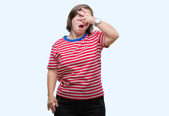 Young adult woman with down syndrome over isolated background peeking in shock covering face and...