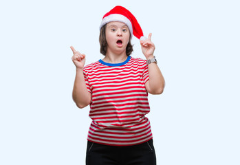 Obraz na płótnie Canvas Young adult woman with down syndrome wearing christmas hat over isolated background amazed and surprised looking up and pointing with fingers and raised arms.