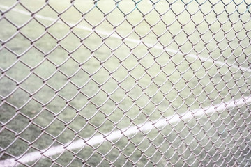 Tennis court fencing with mesh netting against the background of the court and marking with white paint