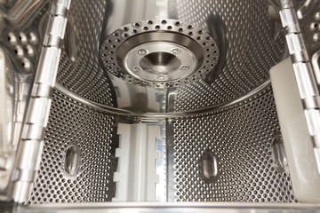 The drum of the washing machine with a vertical load, top-loading, inside view. Internal drum cover made of stainless steel with perforated and convex holes. Close-up with selective focus