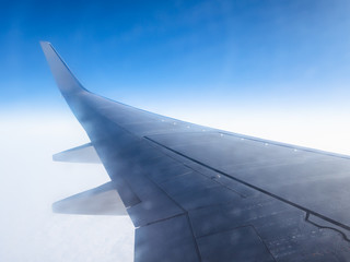 view of airplane wing in blue sky over clouds