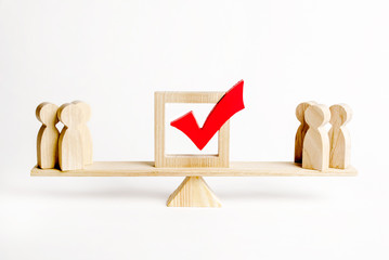Two groups of wooden figures of people and a red check mark on the scales. confrontation of power...