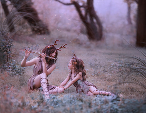 creative fabulous family shooting, faun mom plays lullaby on flute for her child, fairytale characters deer in long brown dresses are relaxing in clearing, art photo for mother's day, parents care