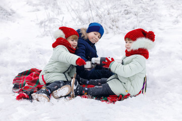Children are sitting on a plaid and pouring tea from the thermos