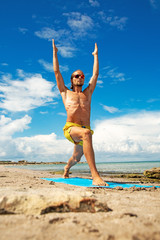 athletic man on beach doing fitness yoga exercise. Acroyoga element for strength and balance.