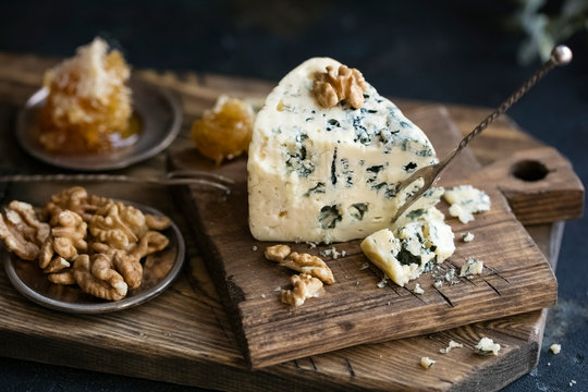 Danish blue cheese on a wooden board with walnut kernels. dark background