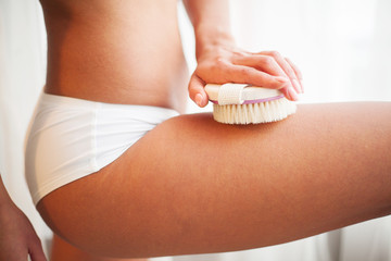 Woman's arm holding dry brush to top of her leg. Cellulite treatment, dry brushing