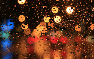 Raindrops on the car windshield with blurred signboard lights along the urban street at night 